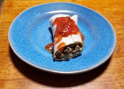 A breakkfast burrito topped with salsa on a plate.